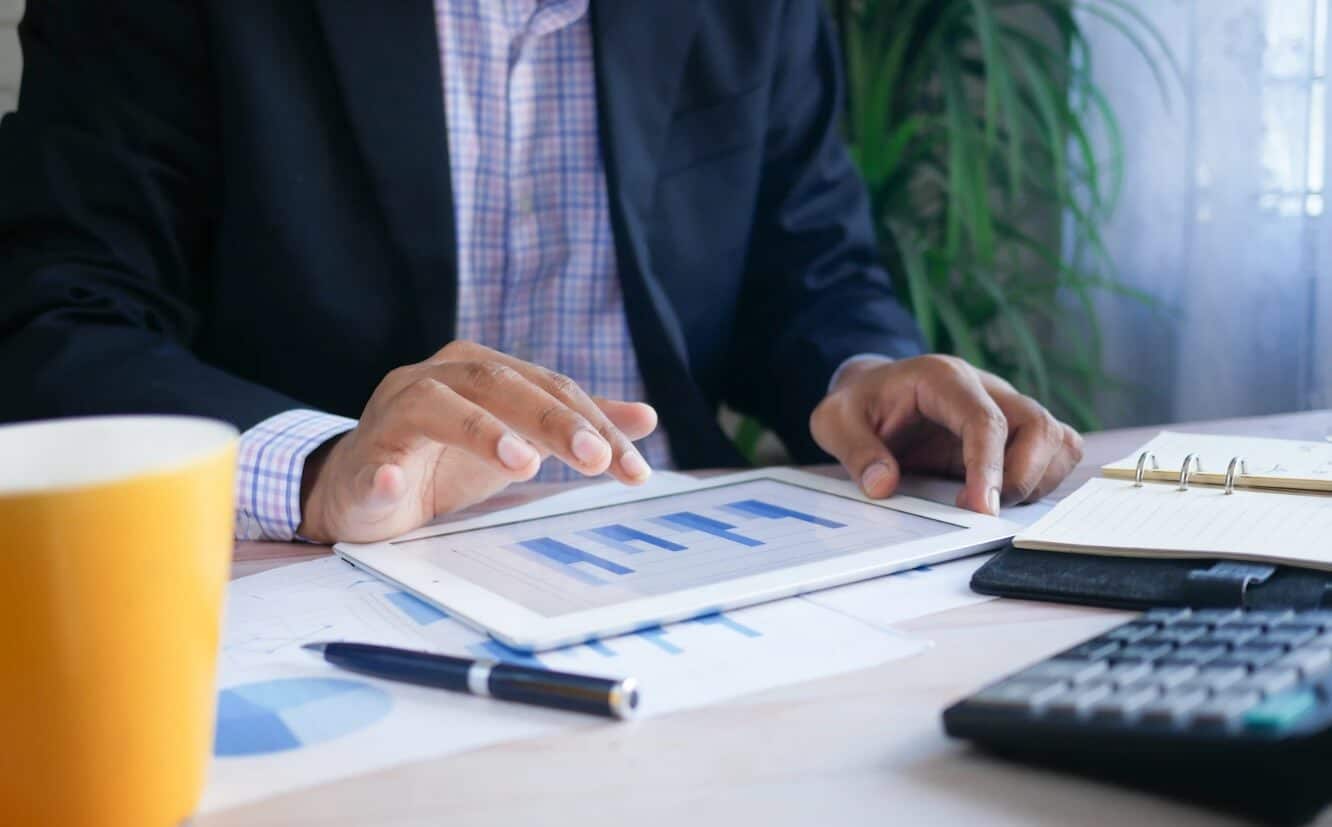 man sitting at table looking at tablet with trading chart