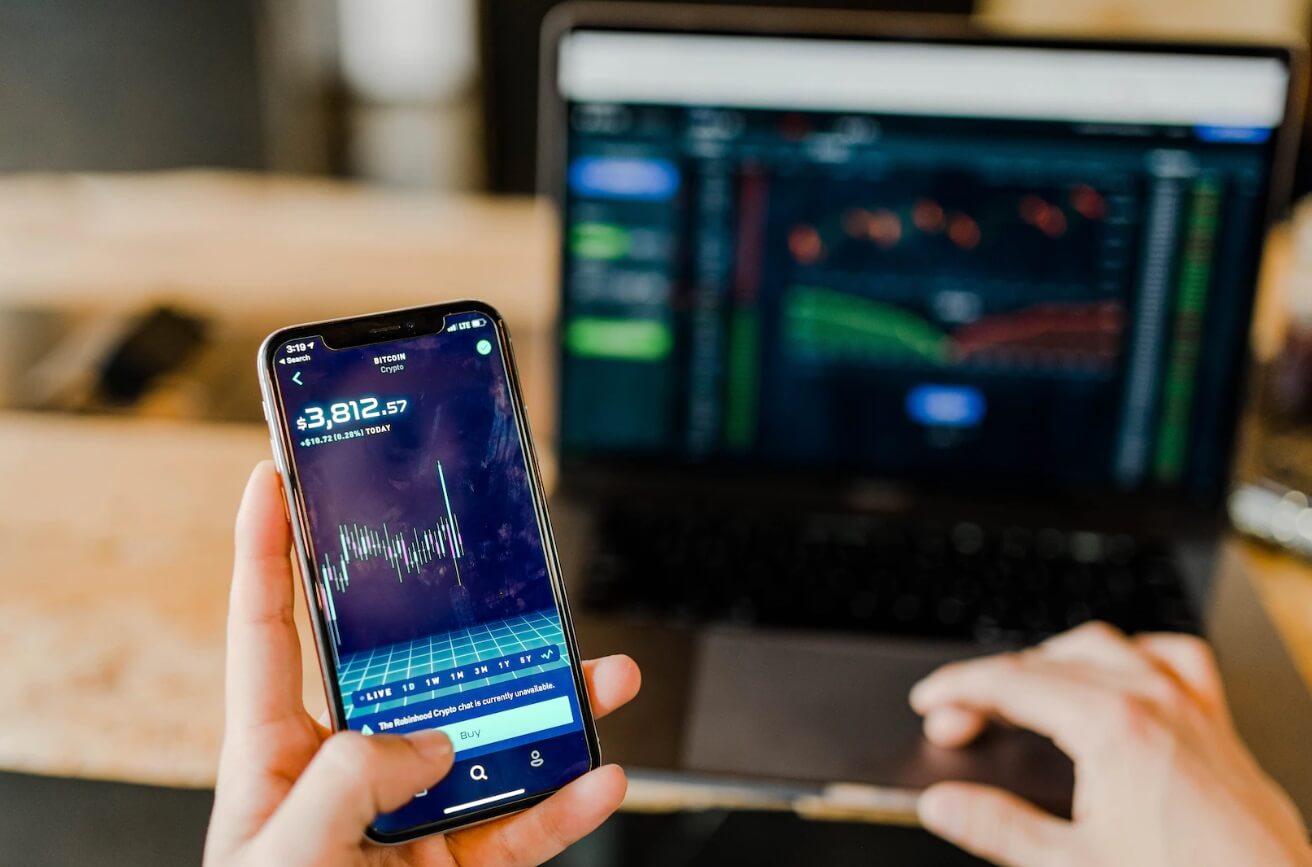 hand holidng phone with laptop in background showing forex chart