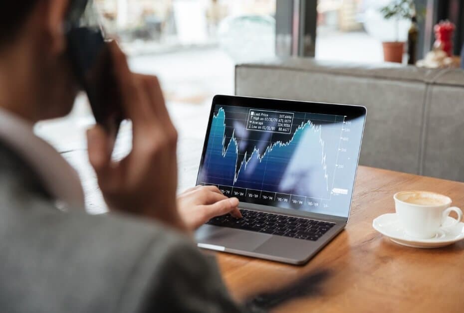 man having coffe looking over laptop showing trading chart