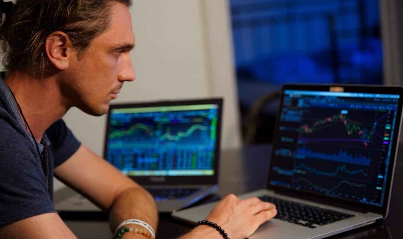man looking at trading chart on two laptops