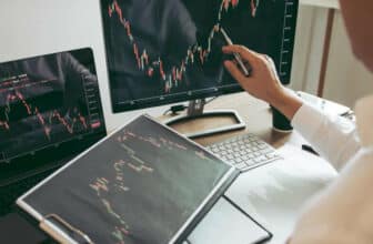 person holding tablet, and going over trade on PC screen