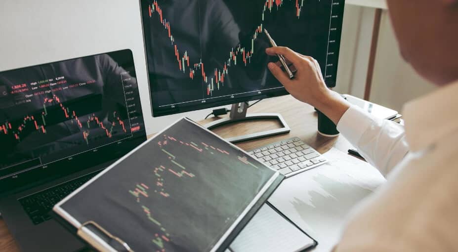 person holding tablet, and going over trade on PC screen